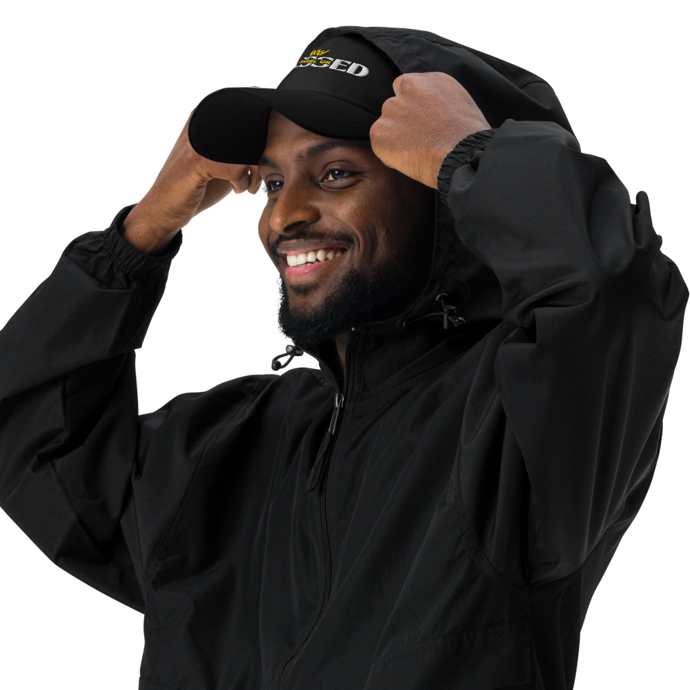 Close up image of a smiling person putting a hood over the peak of a baseball cap with blessed apparel logo in yellow and white.