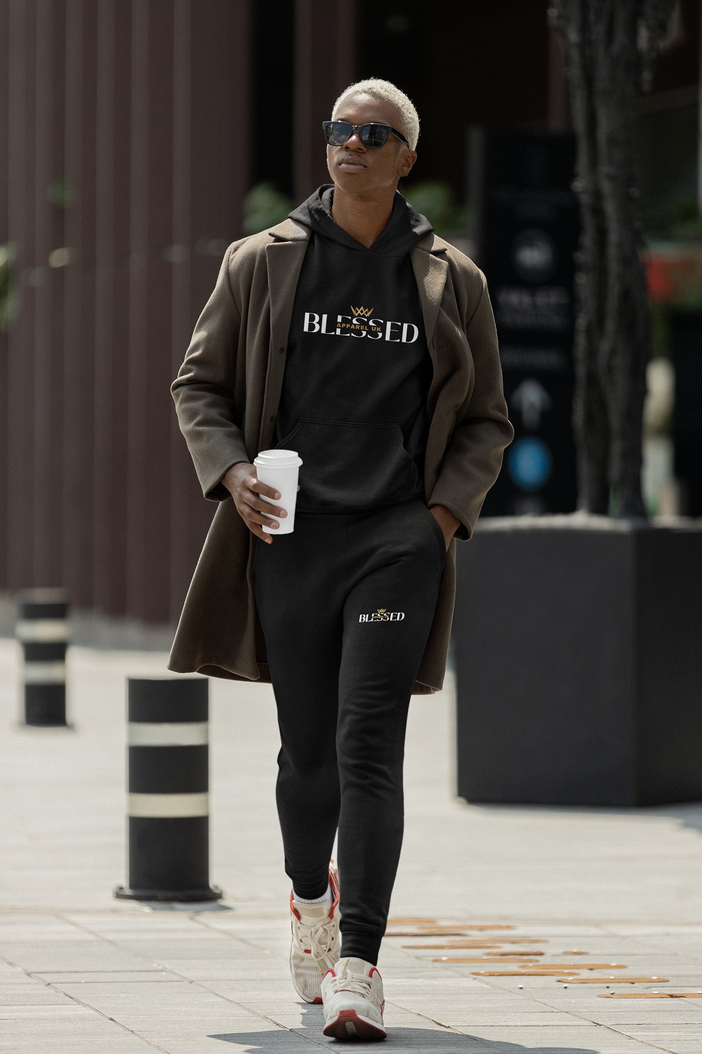 Image of a person walking down the street wearing black hoodie and sweatpants with blessed apparel logo in yellow and white.