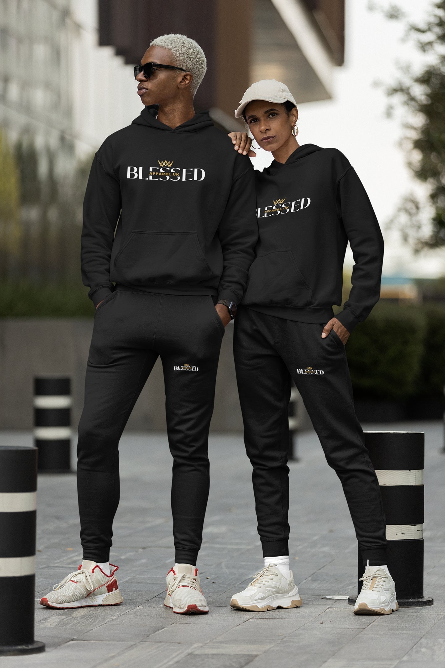 Image of two people wearing black hoodies and sweatpants with blessed apparel logo in yellow and white.