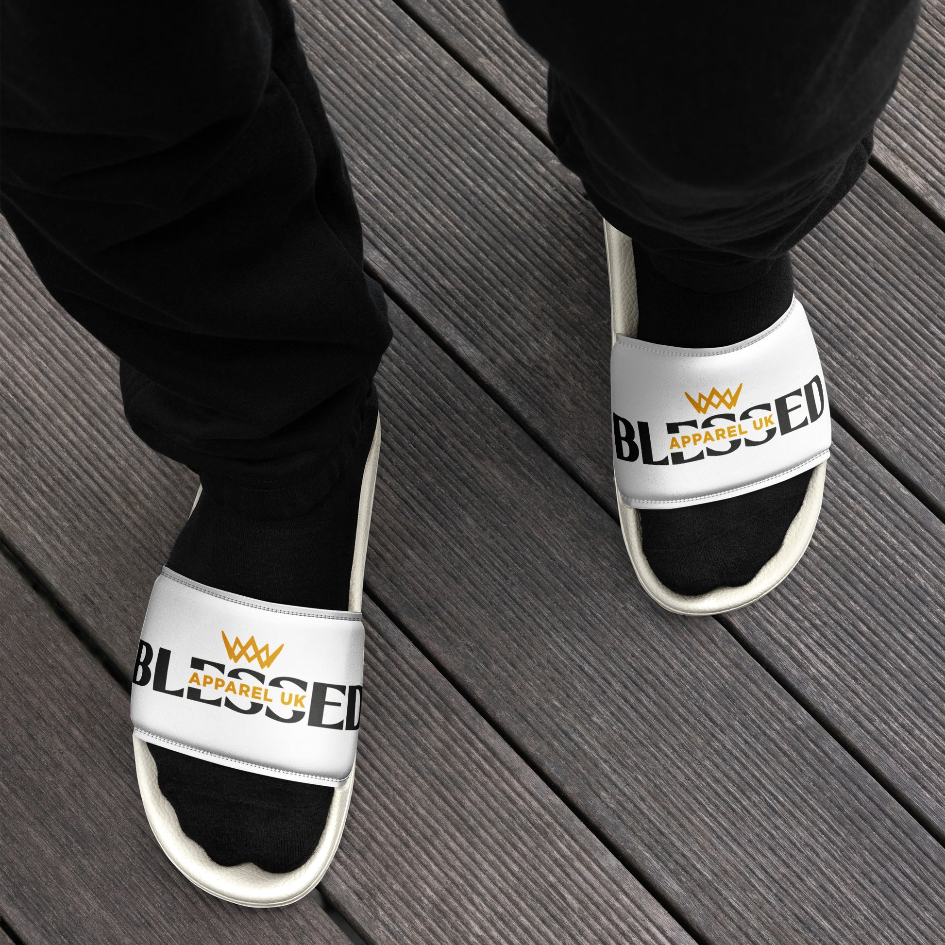 Close up image of a person 's legs and feet wearing a white pair of slides with blessed apparel logo in yellow and white.