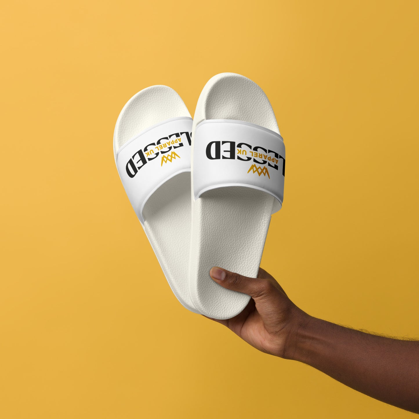 Close up image of a person  holdng a white pair of slides with blessed apparel logo in yellow and white.