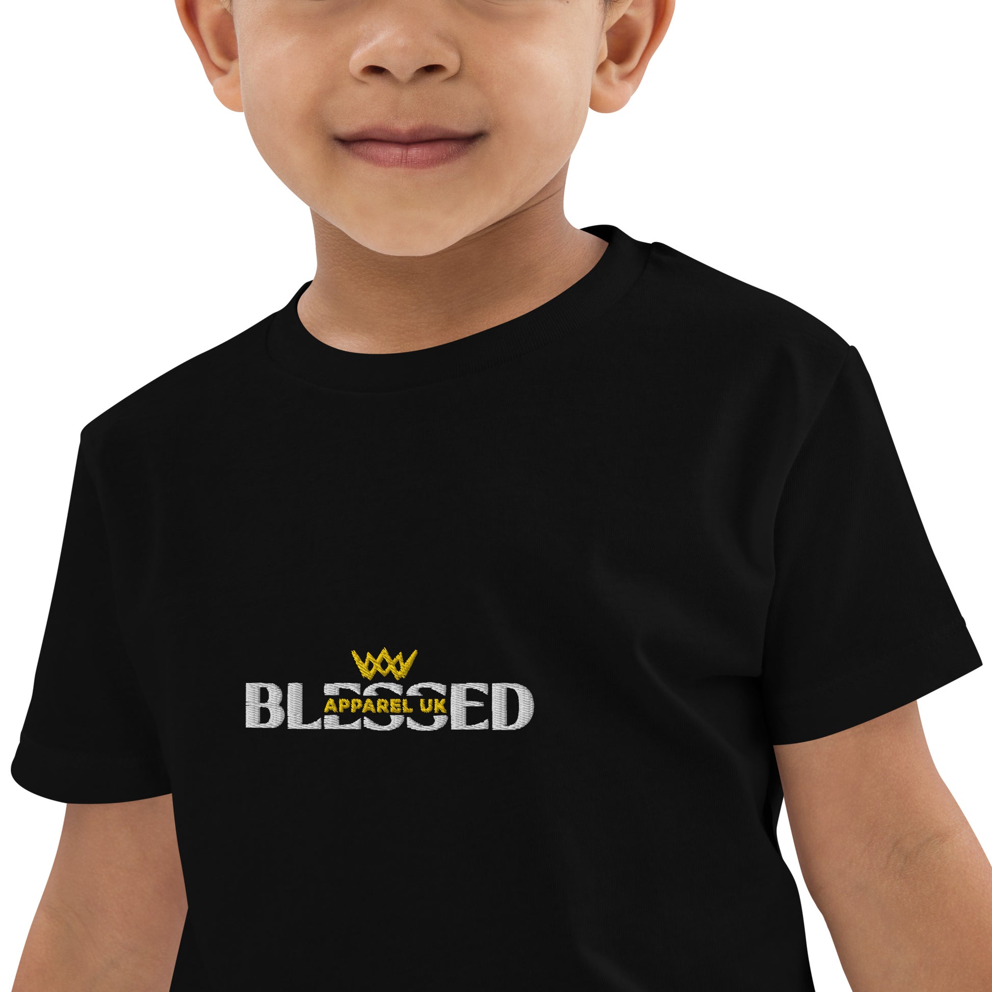 A close-up image of a child wearing a black t-shirt with the Blessed Apparel UK logo in gold and white across the chest.