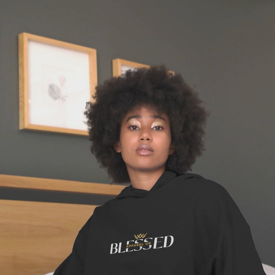 Video of a person sitting on a bed wearing a black hoodie with blessed apparel logo in yellow and white.