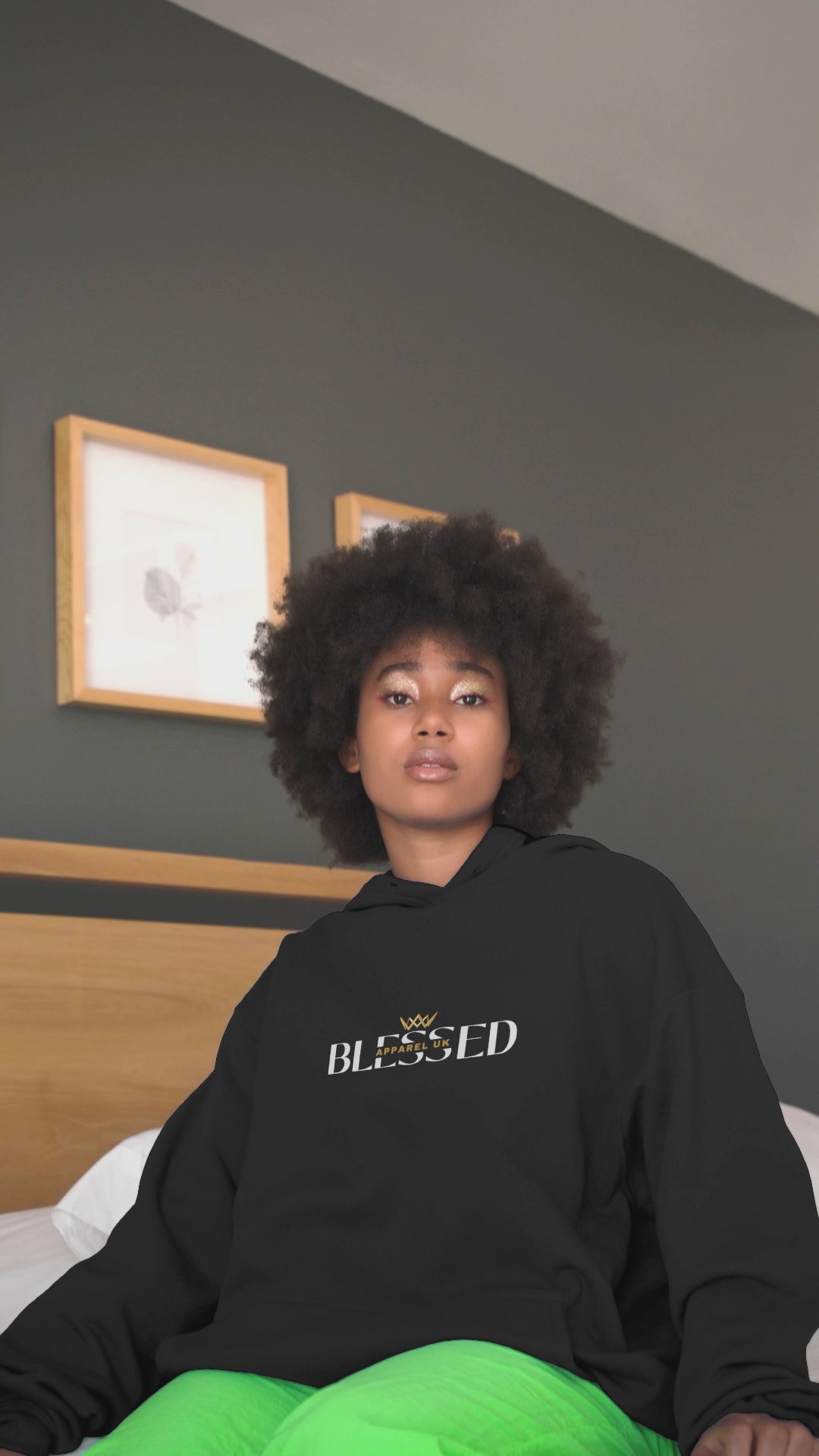 Video of a person sitting on a bed wearing a black hoodie with blessed apparel logo in yellow and white.